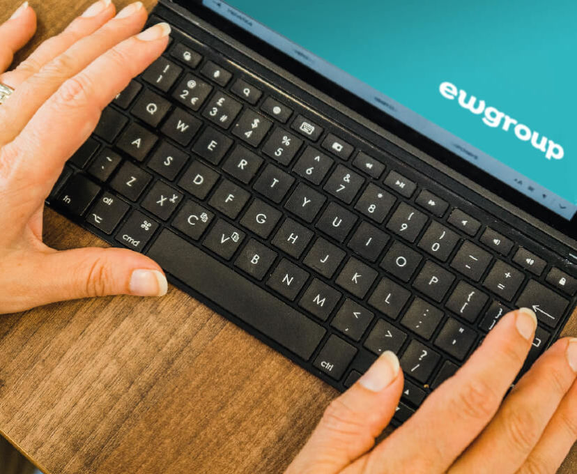 Inclusive Recruitment course - keyboard with hands, EW logo on teal coloured screen
