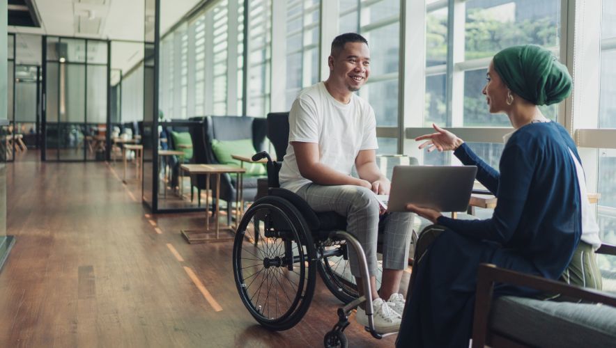 Disability recruitment - Man in wheelchair speaking with seated woman in head scarf