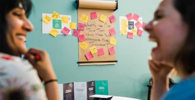 Two people out of focus having a conversation in front of a board with sticky notes,